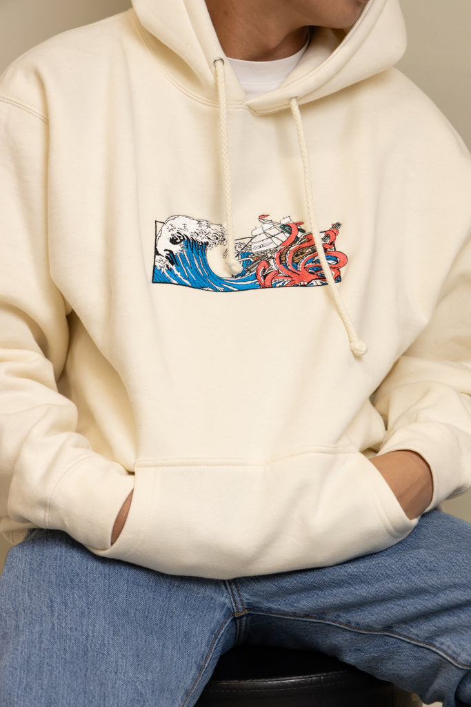 A close up view of a man wearing cream Squid Industries x Simple Stock Hoodie posing