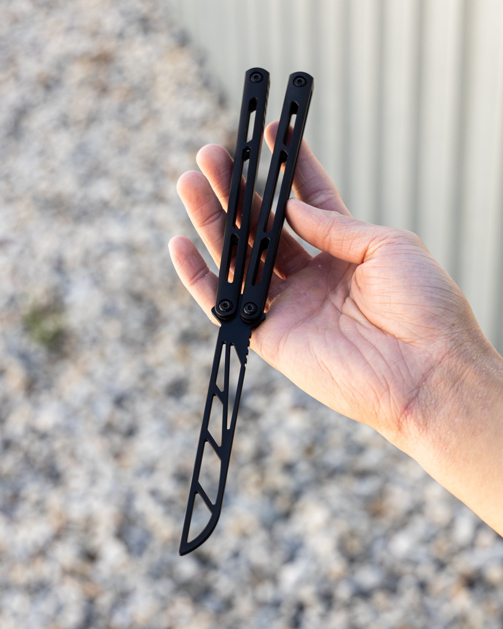Hand holding a black folding knife against a blurred outdoor background