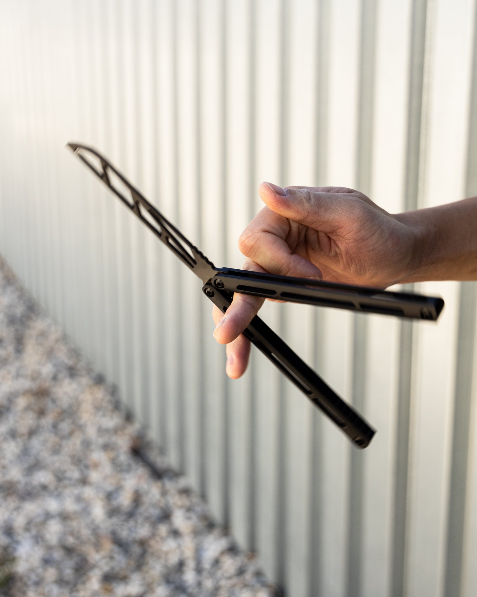 Hand flipping a trainer balisong against a corrugated metal background