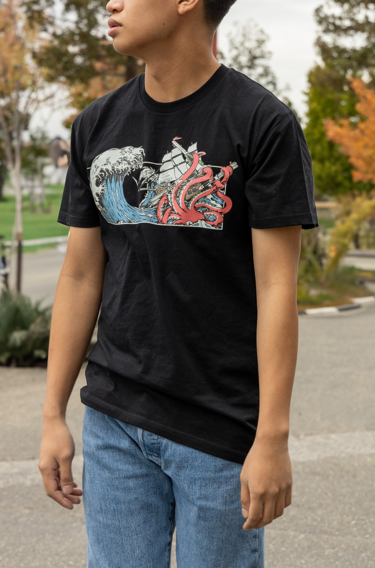 Man wearing a Squid Industries x Simple Stock Collaboration Black T-shirt featuring a Kraken in Tsunami waves holding on the Squid Industries balisongs