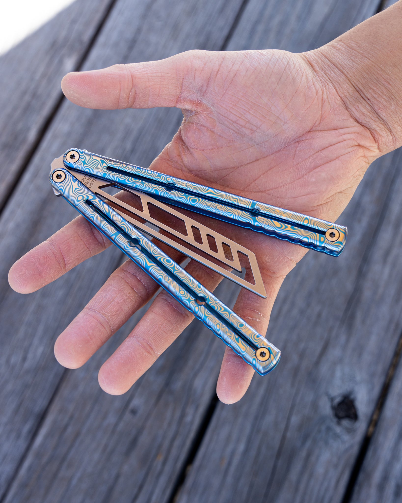 hand holding a blue engraved damascus titanium krake raken 