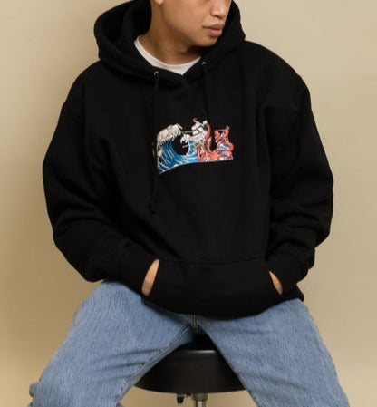 Man wearing a Black Squid Industries x Simple Stock Hoodie posing while sitting on a chair