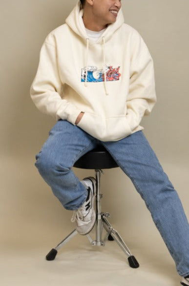 Man wearing cream Squid Industries x Simple Stock Hoodie posing while sitting on a chair 